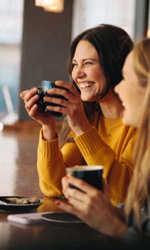 Two women having coffee and smiling. Happy female friends having a great time together in a cafe.